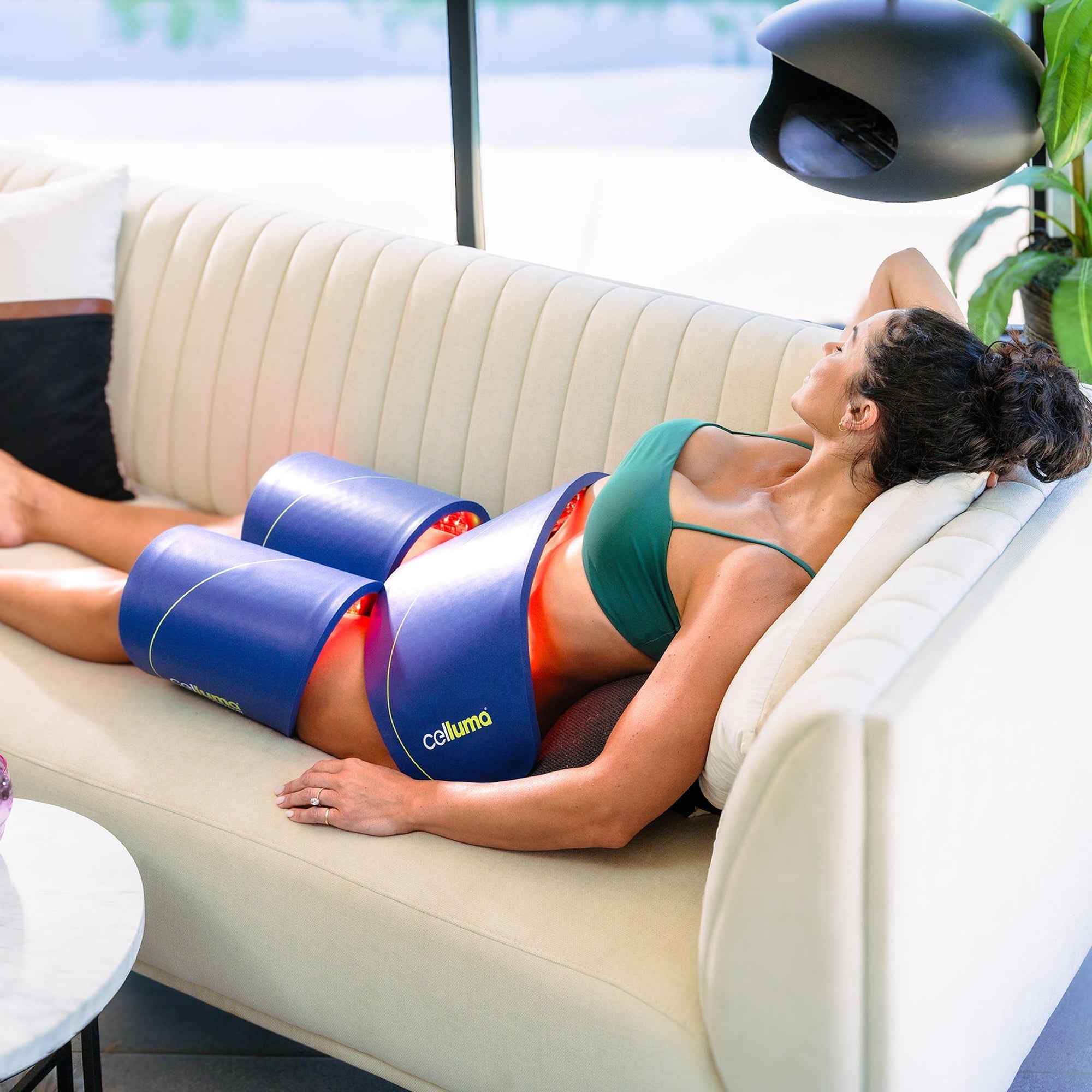 Woman using Celluma contour led red light therapy system to do body contouring for firming her belly and thighs. 