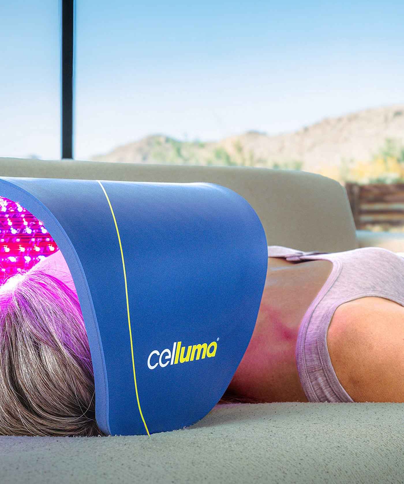 Woman using a Celluma PRO PLUS LED red light therapy on a couch doing skin rejuvenation.