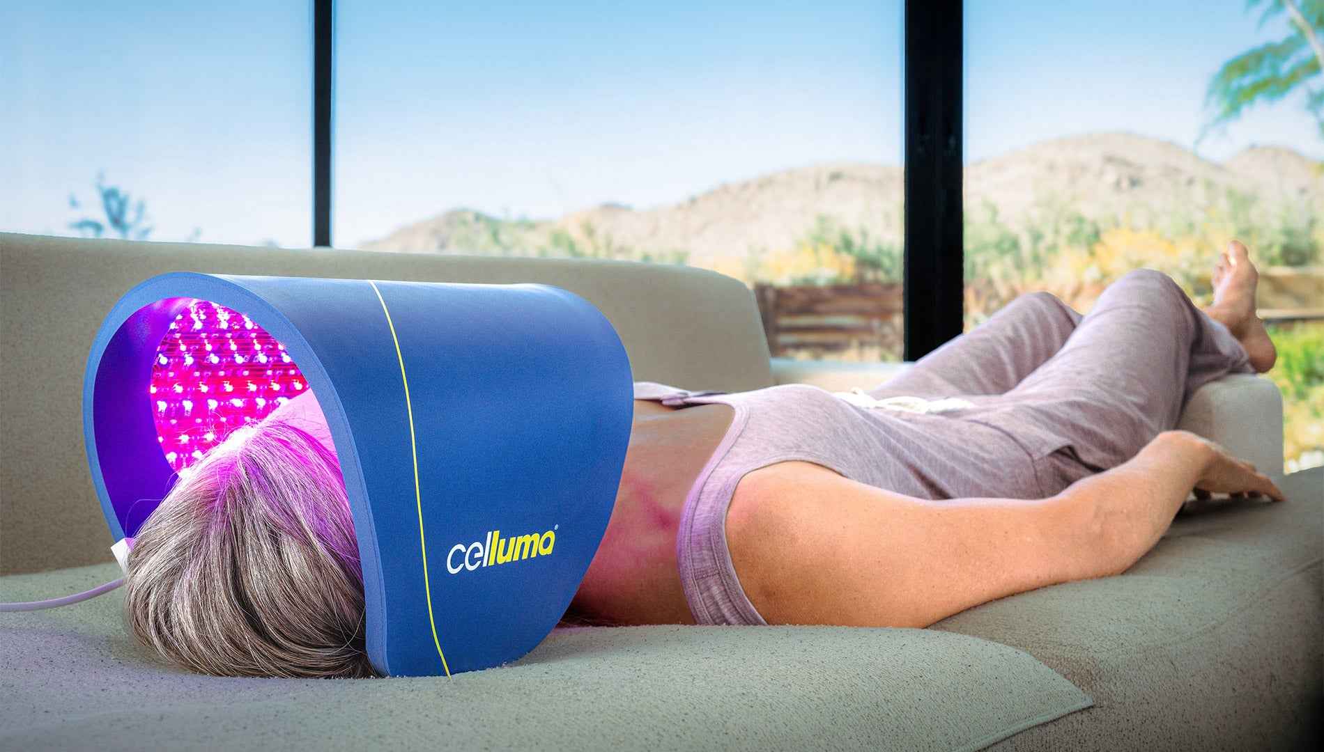 Woman using a Celluma PRO PLUS LED red light therapy on a couch doing skin rejuvenation.
